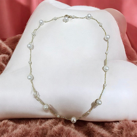 001 - Pearl necklace (304705) displayed on a white cushion with a pink background. The pearls are evenly spaced on the chain.